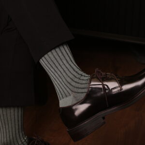 Elegant man wearing light Mint ribbed luxury socks paired with polished dark brown oxford shoes and black trousers, sitting indoors on wooden floor — sophisticated men’s fashion accessory style by Celchuk Luxury Socks.